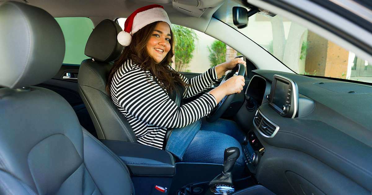 Smiling woman with a Santa hat sitting in the driver's seat of a car.