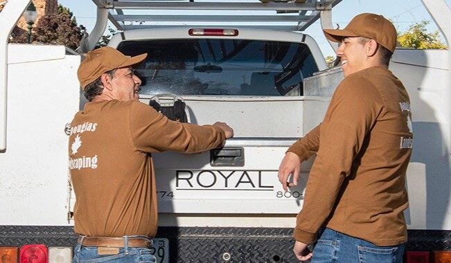 Father and son stand next to the tailgate of a landscaping truck owned by their family business.